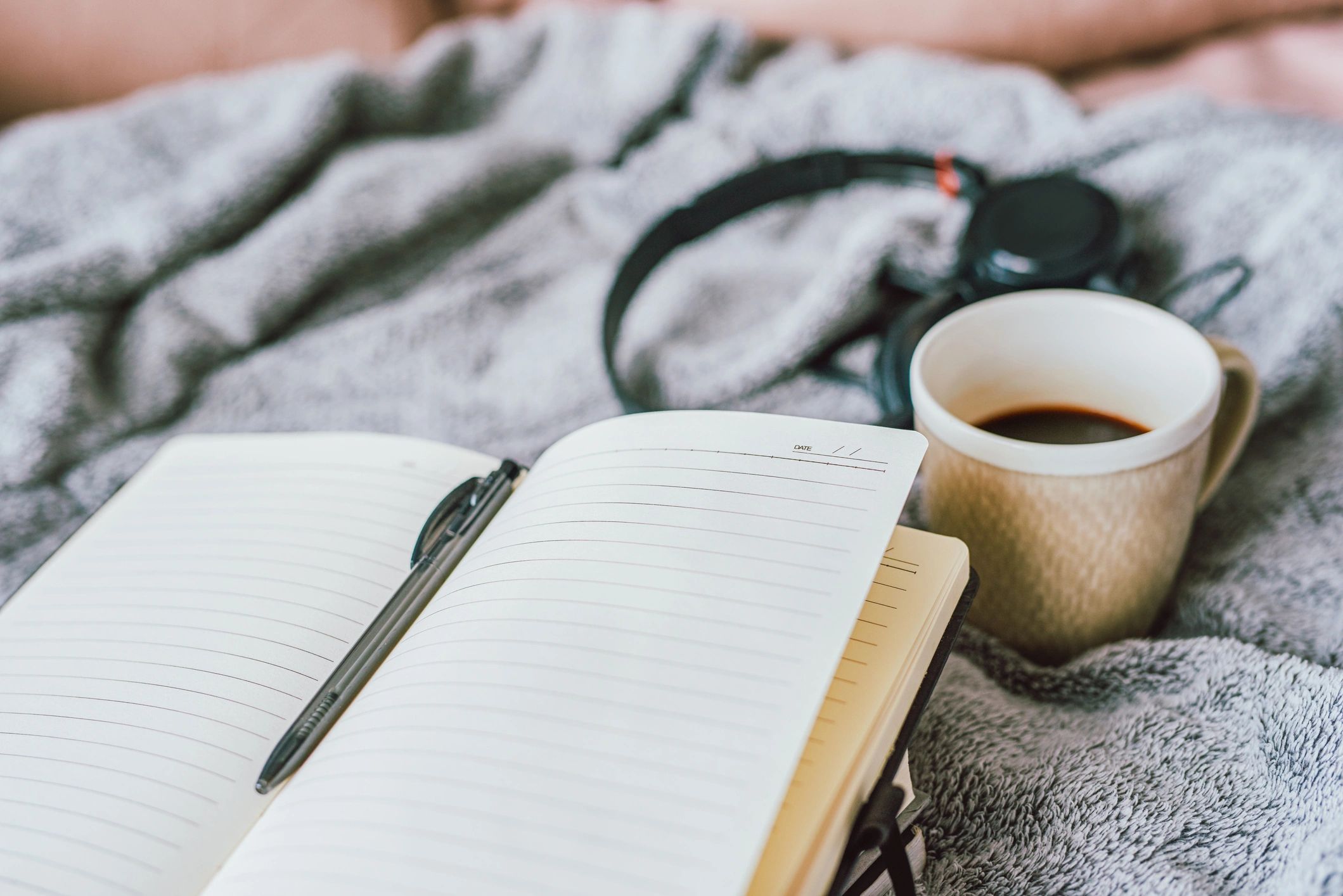 Notebook, coffee, and headphones arranged on a cozy surface